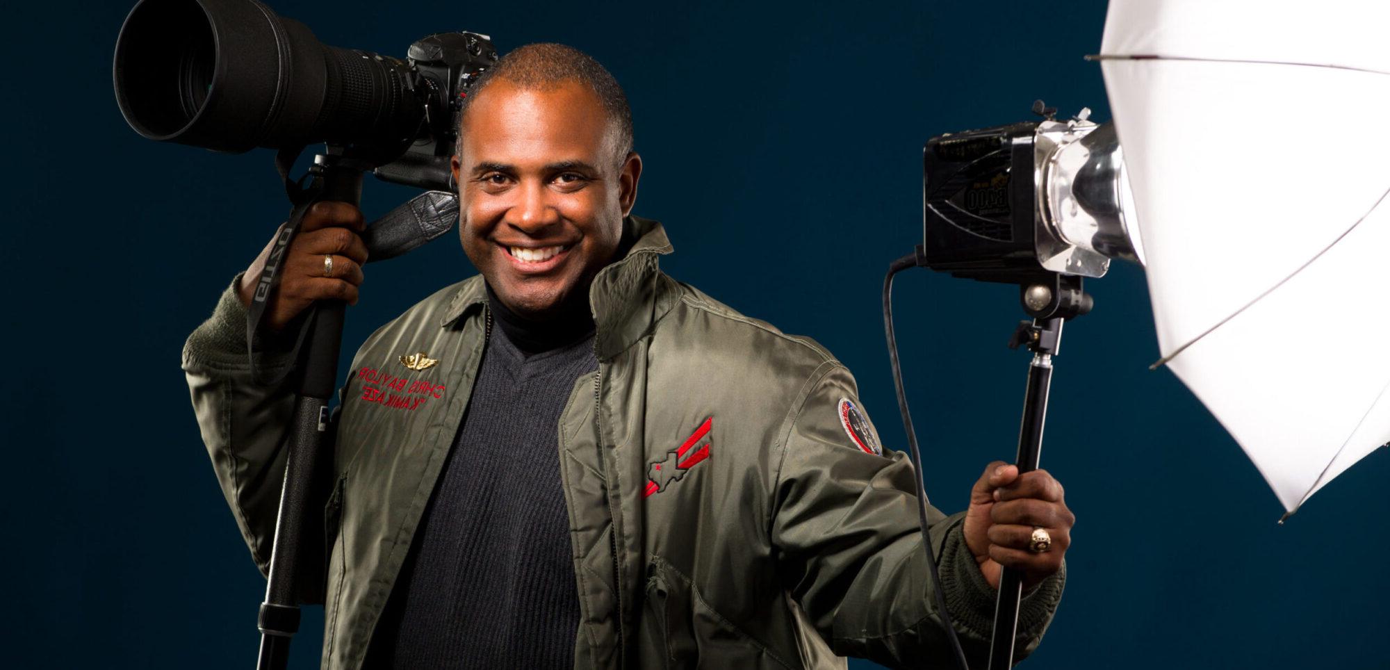 Black male photographer with with camera and strobe in hand.