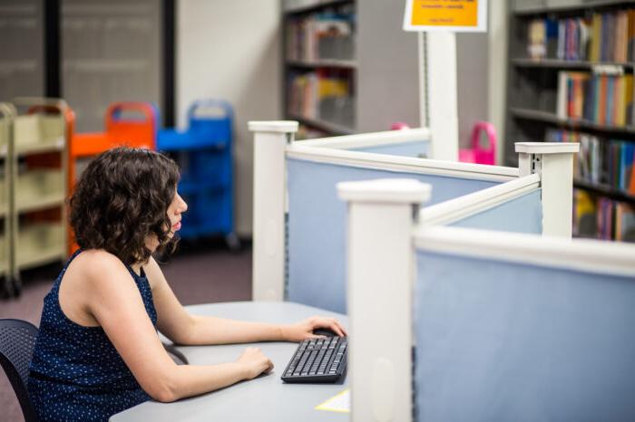 一名身着蓝色衣服的女性在计算机实验室的电脑前工作.