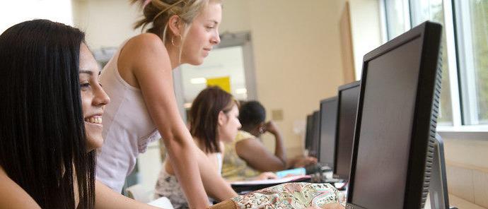 A female student looking at the computer along with other students at different computers.