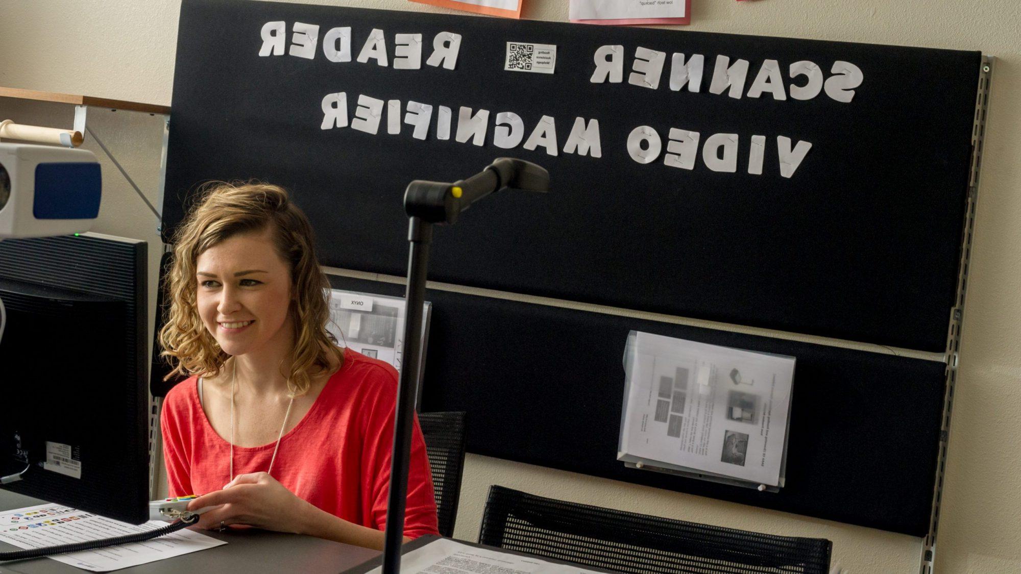 A female student in front of a sign that says scanner reader video magnifier.