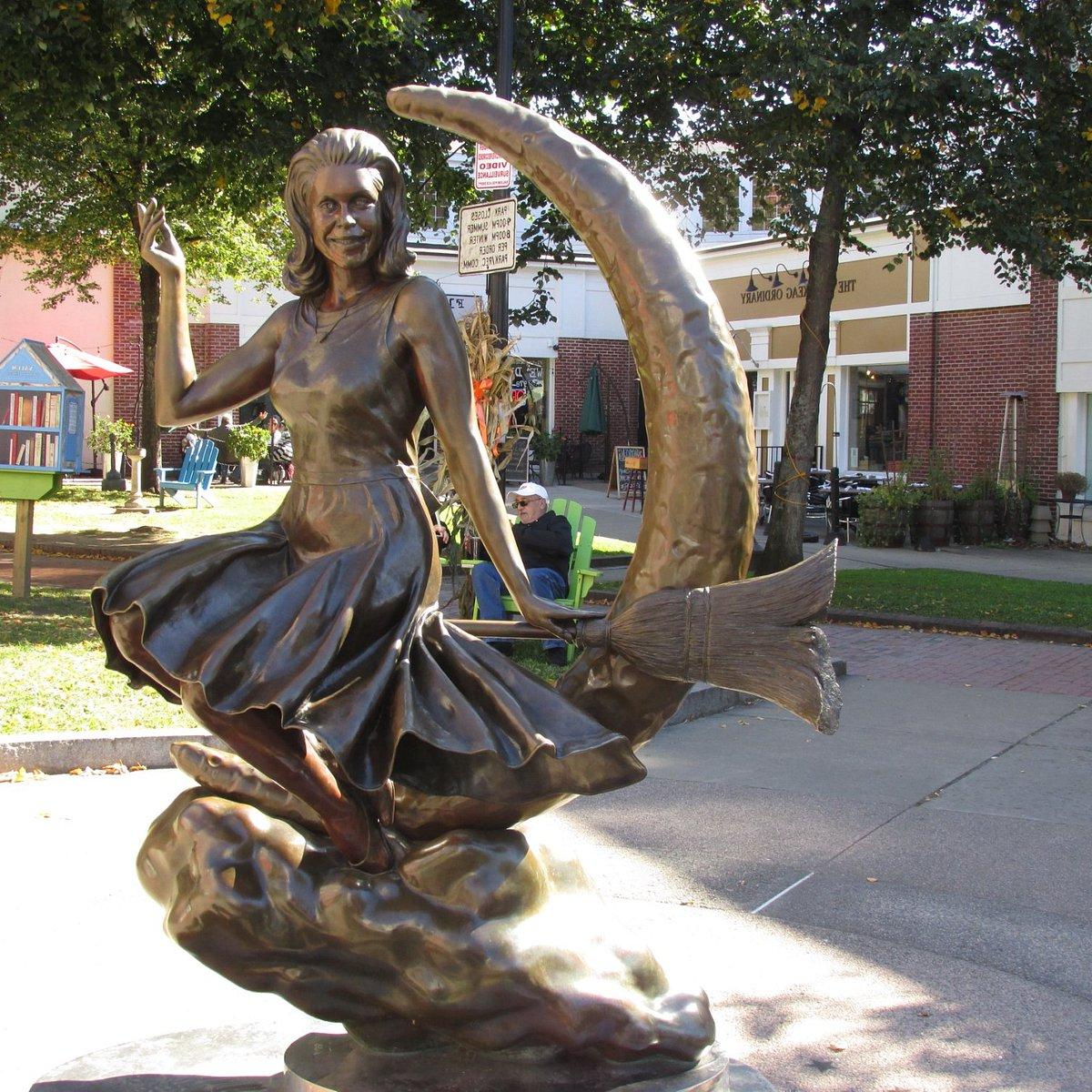 A bronze statue of a woman riding a broom in front of a crescent moon